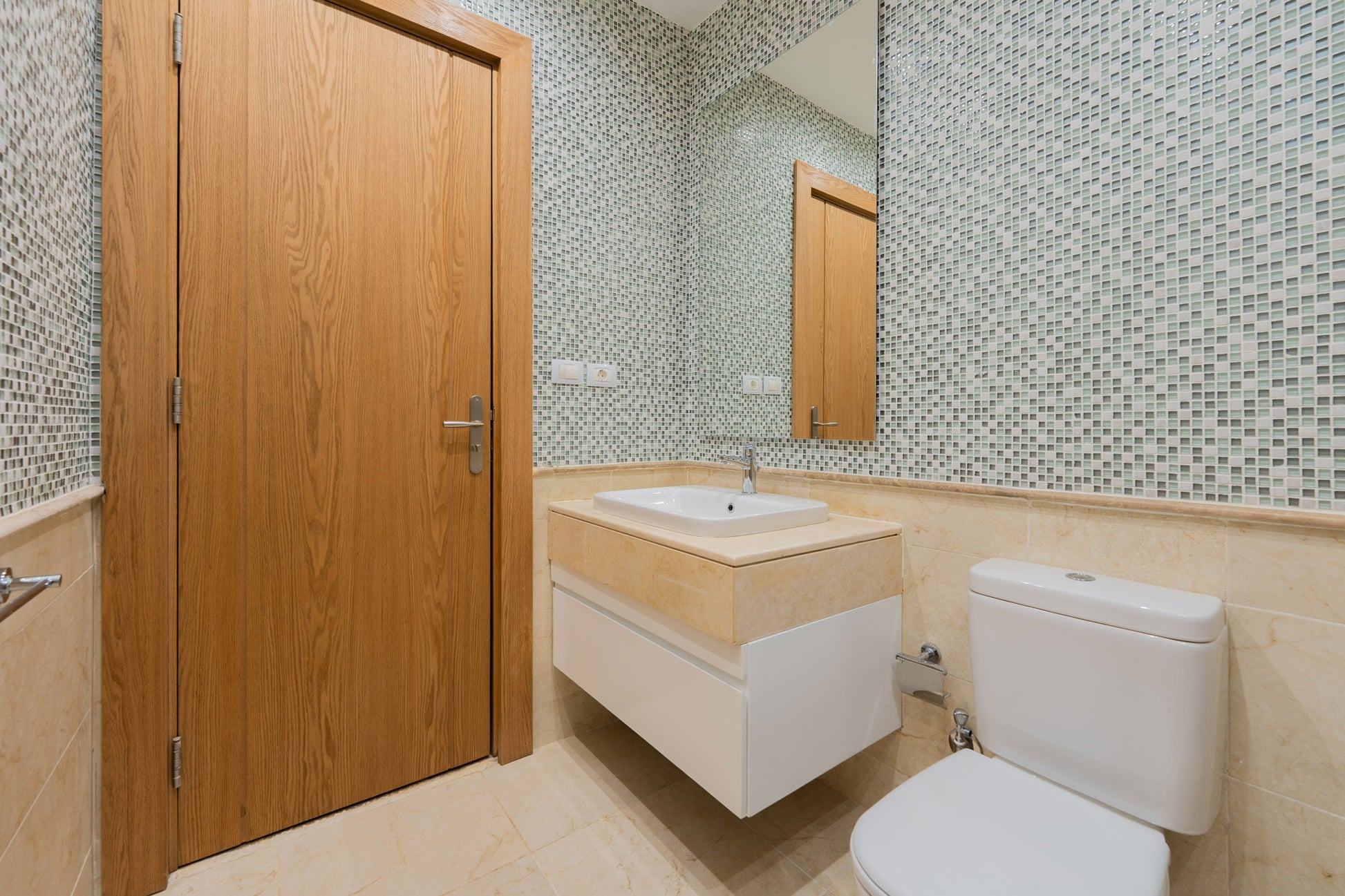 This image features a modern bathroom setting, showcasing a sleek beige marble countertop with integrated white cabinetry. Above the sink, a large rectangular mirror with a slim profile reflects the stylish interior.